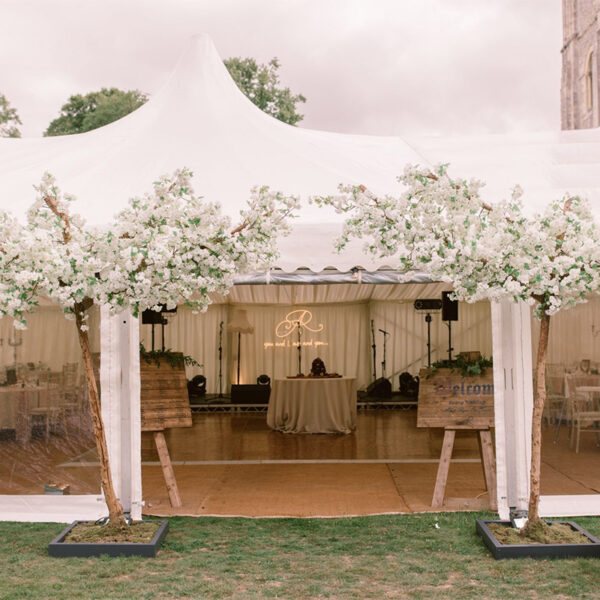 Artificial white blossom tree arch creating entrance to a marquee